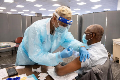 A Howard University health worker in personal protective equipment administering a vaccine to a patient.